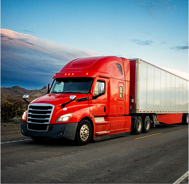 A large red transport truck in motion with a light blue sky in the background 